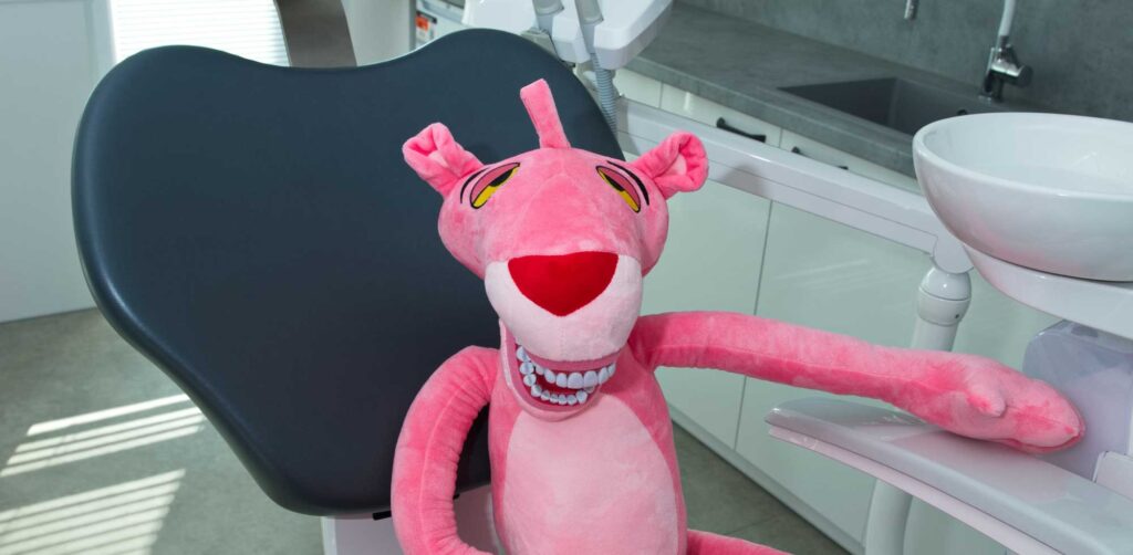 Plyšový Růžový panter sedí v zubním křesle v ordinaci.